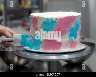 chef pastry designer confectioning a frosted 3 floor layered cake decorated with pastel creamy colors photo. Stock Photo