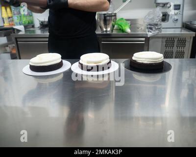 chef pastry designer confectioning a frosted 3 floor layered cake stuffed with strawberries , blueberries and whipped butter cream. Cake structure bef Stock Photo