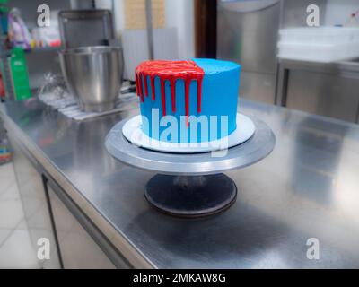 blue sprayed frosted cake on stand dripped with red ganache filling and white meringues and whipper cream on top Stock Photo