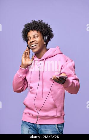 Happy African teenager wearing headphones using mobile dancing listening music. Stock Photo