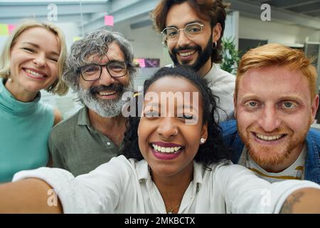 Colleagues looking at the camera taking selfie with cheerful expression.  Stock Photo