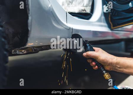 Close-up of male hand holding small rotary saw tool cutting out fragment of body of car. Garage work. Horizontal indoor shot. High quality photo Stock Photo