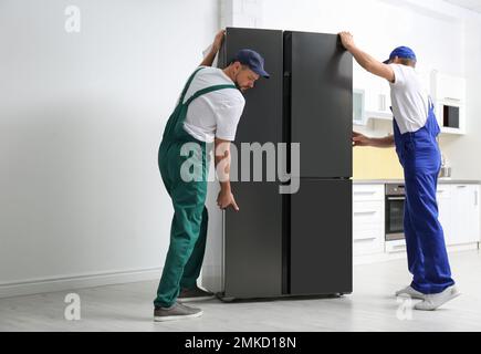 Professional workers carrying modern refrigerator in kitchen Stock Photo
