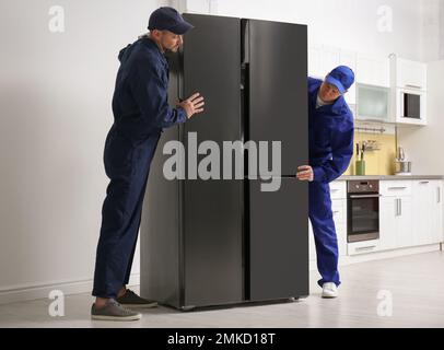 Professional workers carrying modern refrigerator in kitchen Stock Photo