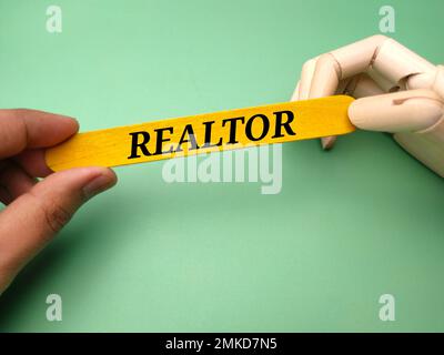 Someone hand and wooden hand together holding colored wood with word REALTOR. Stock Photo