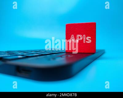 Red block and black keyboard with the word APIs on blue background. Stock Photo