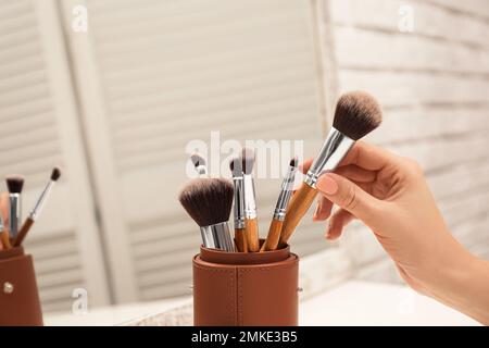 Professional makeup artist taking brush on dressing table, closeup Stock Photo