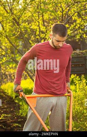 A farmer man works in the field, plowing the land with a plow on the farm. A plowman on a walk behind a motor cultivator. Tillage season. Organic cult Stock Photo