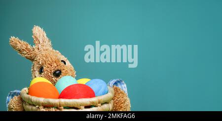 Easter colorful eggs in a straw bunny basket on green blue background. Soft Fokus. Copy space. Close up Stock Photo