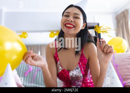 Happy biracial woman having party at home making video call and smiling, copy space. Celebration, party and communication concept. Stock Photo