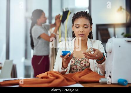 Which colour...a young fashion designer sewing garments while a colleague works on a mannequin in the background. Stock Photo