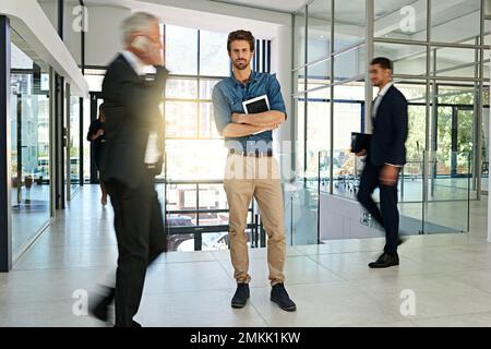 Hes a young mover and shaker in the company. Portrait of a smiling young businessman standing in a busy office. Stock Photo