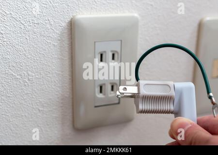 A Japanese wall socket without earth post. 3 pins power plug connected to a travel adapter. Stock Photo