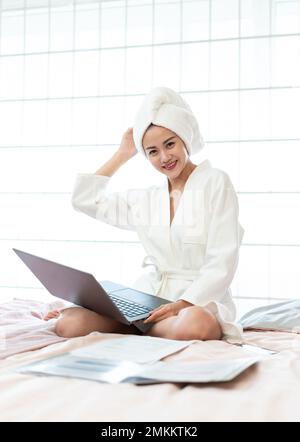 A young woman wearing a bathrobe to use a computer on the bed Stock Photo