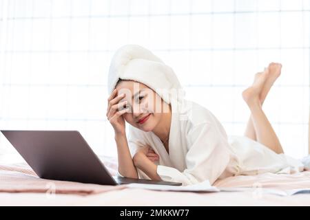 A young woman wearing a bathrobe to use a computer on the bed Stock Photo