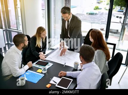 Hes got a clear vision for the new building plan. a team of architects going over a blueprint during a formal meeting in an office. Stock Photo