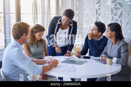 Running numbers by her team. a group of colleagues discussing paperwork together at a table in an office. Stock Photo
