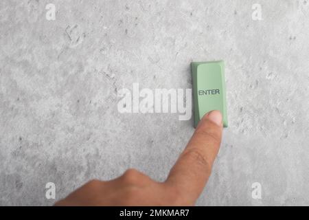 Finger pressing Enter button on gray background.Copy space. Stock Photo