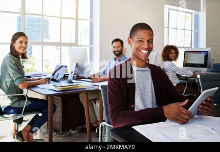 We love working in an open and transparent work environment. Portrait of a young man using a digital tablet at his desk in a modern office. Stock Photo