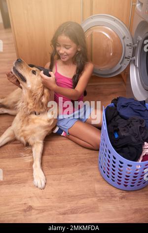 Chore day is childs play. a young girl doing laundry at home while her dog keeps her company. Stock Photo