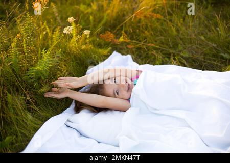 Girl sleeps on bed in grass, Sweet stretches and yawns sleepily, good morning in fresh air. Eco-friendly, healthy sleep, Protection from mosquitoes, c Stock Photo