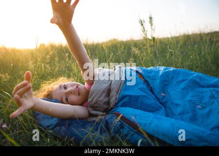 A child sleeps in a sleeping bag on the grass in a camping trip - eco-friendly outdoor recreation, healthy lifestyle, summer time. Sweet and peaceful Stock Photo