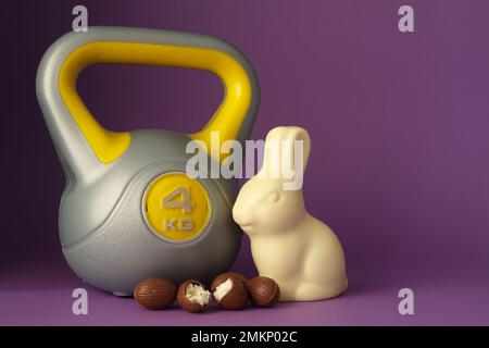 Kettlebell, chocolate Easter bunny and eggs. Gym workout, fitness composition. Cheat day or healthy diet choice, weight loss concept with copy space. Stock Photo