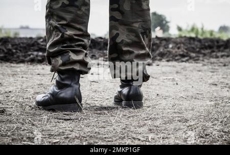 Soldier legs on a battlefield, wearing military boots and woodland camo pants, camouflage trousers. Stock Photo