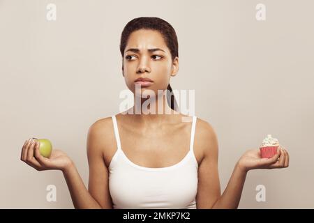 Lovely african american woman makes a choice between cake and apple on white Stock Photo