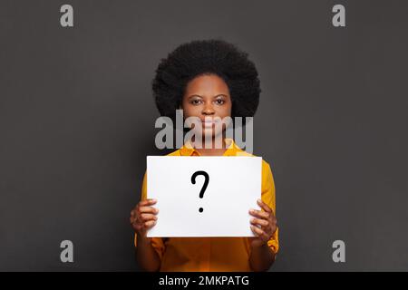 Cheerful african american woman showing card with question mark on black background. Idea concept Stock Photo