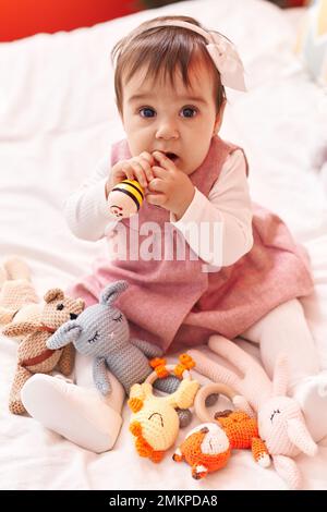 Adorable hispanic baby bitting maraca sitting on bed at bedroom Stock ...
