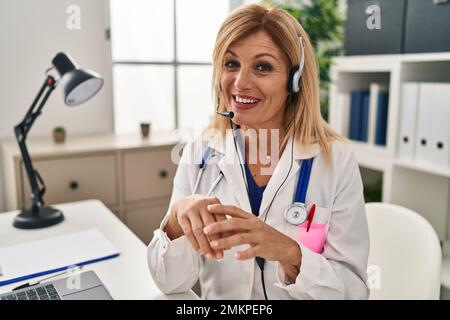 Middle age blonde woman wearing doctor uniform having medical teleconsultation at clinic Stock Photo