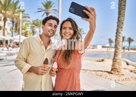 Man and woman couple eating ice cream and make selfie by the smartphone at seaside Stock Photo