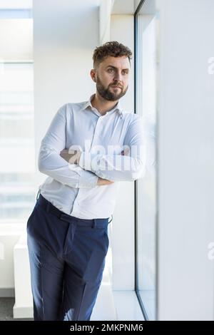 Portrait of a business young successful man in a modern office standing by the window against the backdrop of the city Stock Photo