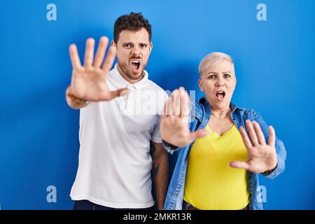 Young brazilian mother and son standing over blue background doing stop gesture with hands palms, angry and frustration expression Stock Photo