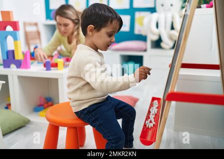 Teacher and toddler writing on blackboard at kindergarten Stock Photo