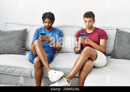 Two men friends using smartphone sitting on sofa at home Stock Photo