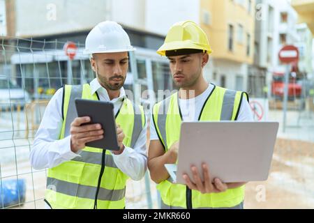 Two hispanic men architects using touchpad and laptop working at street Stock Photo