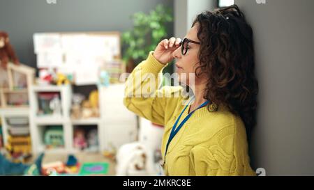 Middle age hispanic woman preschool teacher stressed standing at kindergarten Stock Photo