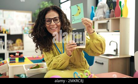 Middle age hispanic woman preschool teacher having vocabulary lesson at kindergarten Stock Photo