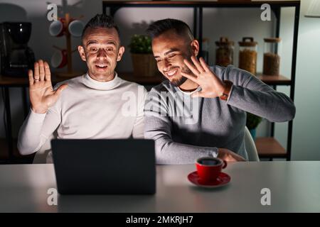 Homosexual couple using computer laptop waiving saying hello happy and smiling, friendly welcome gesture Stock Photo