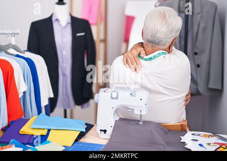 Middle age man with grey hair dressmaker using sewing machine hugging oneself happy and positive from backwards. self love and self care Stock Photo
