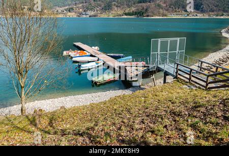 Lake Ledro (Ledro Valley) and the surrounding mountains on a clear spring day. A boat landing stage and some boats. Trento province, northern Italy Stock Photo