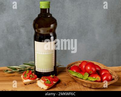 The typical Italian bruschetta with toasted bread, tomato, basil and olive oil on a wooden cutting board and next to it a bottle of extra virgin oil Stock Photo
