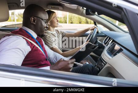 Driving school concept. A car instructor teaches a young woman how to drive. Teaching the rules of the road and driving a vehicle Stock Photo