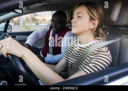 Driving school concept. A car instructor teaches a young woman how to drive. Teaching the rules of the road and driving a vehicle Stock Photo