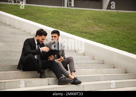 A group of business people meet outdoors. Male employees in suits communicate outdoors. Business partners discuss and argue. Relationships and Stock Photo