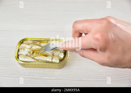 Cropped shot of a man eating a canned of sardines on rustic wooden table Stock Photo