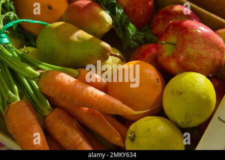 Close up of a bunch of assorted fruit and vegetables with bananas, apples, lemons, pears and carrots in late afternoon light Stock Photo