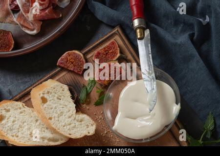 Jamon with figs and a baguette with cream cheese on the dining table, appetizer for wine, Spanish cooking. Stock Photo